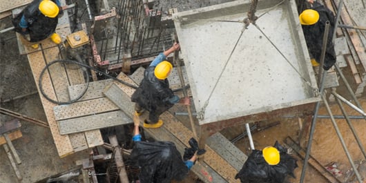 4 trabajadores con cascos, vertiendo cemento bajo la lluvia_600x300_blog